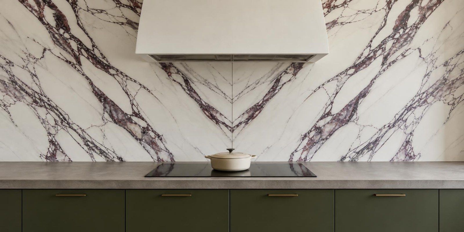 Two marble-look porcelain slabs with purple veins, bookmatched behind an induction cooktop and a white plaster hood