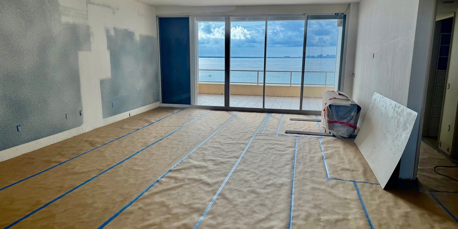A condo living room on Longboat Key mid-job, the floor covered in paper and tape, the bay outside the sliders