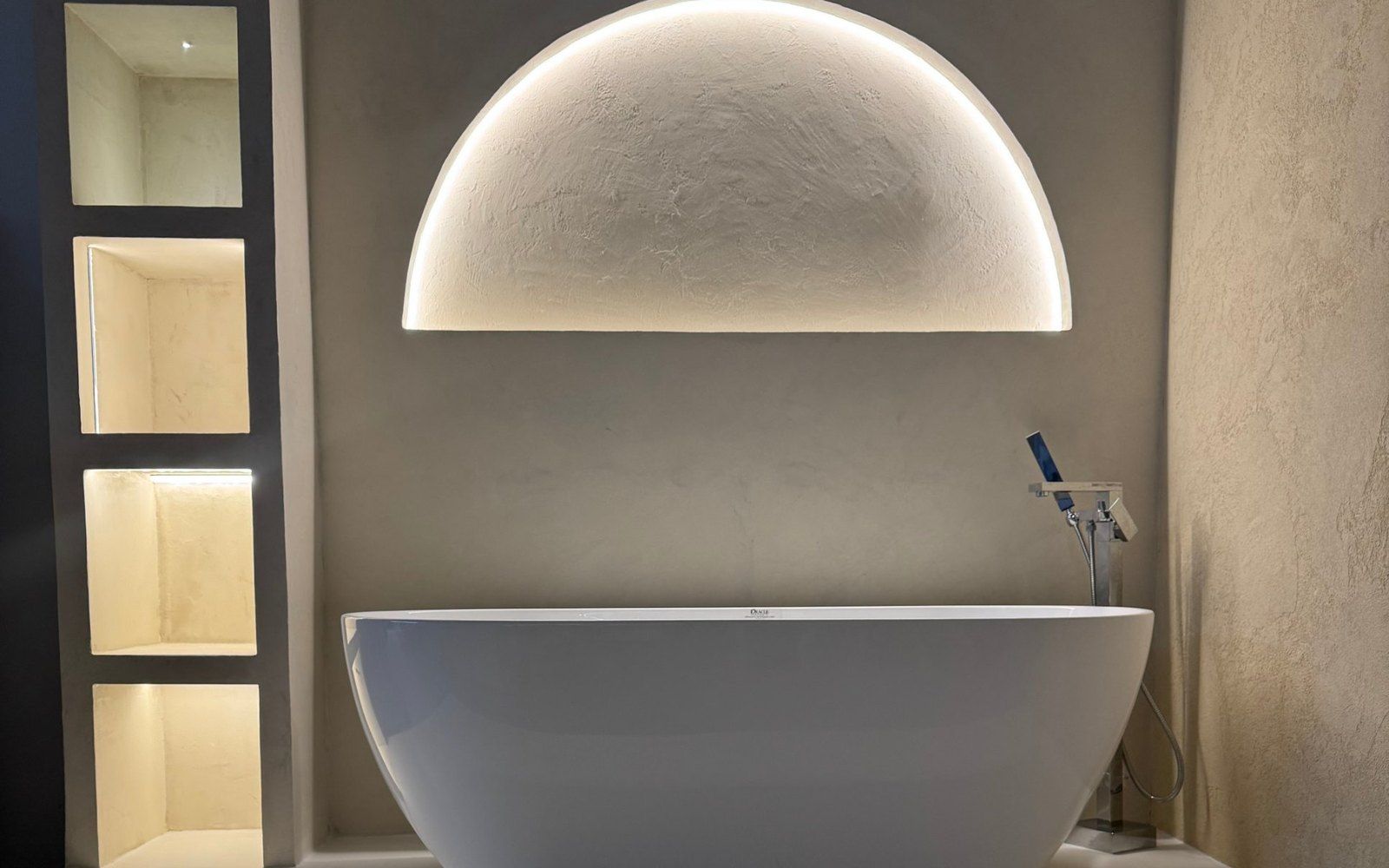 The microcement bath display in our Sarasota showroom: a freestanding tub, lit niches and an arch, all in microcement