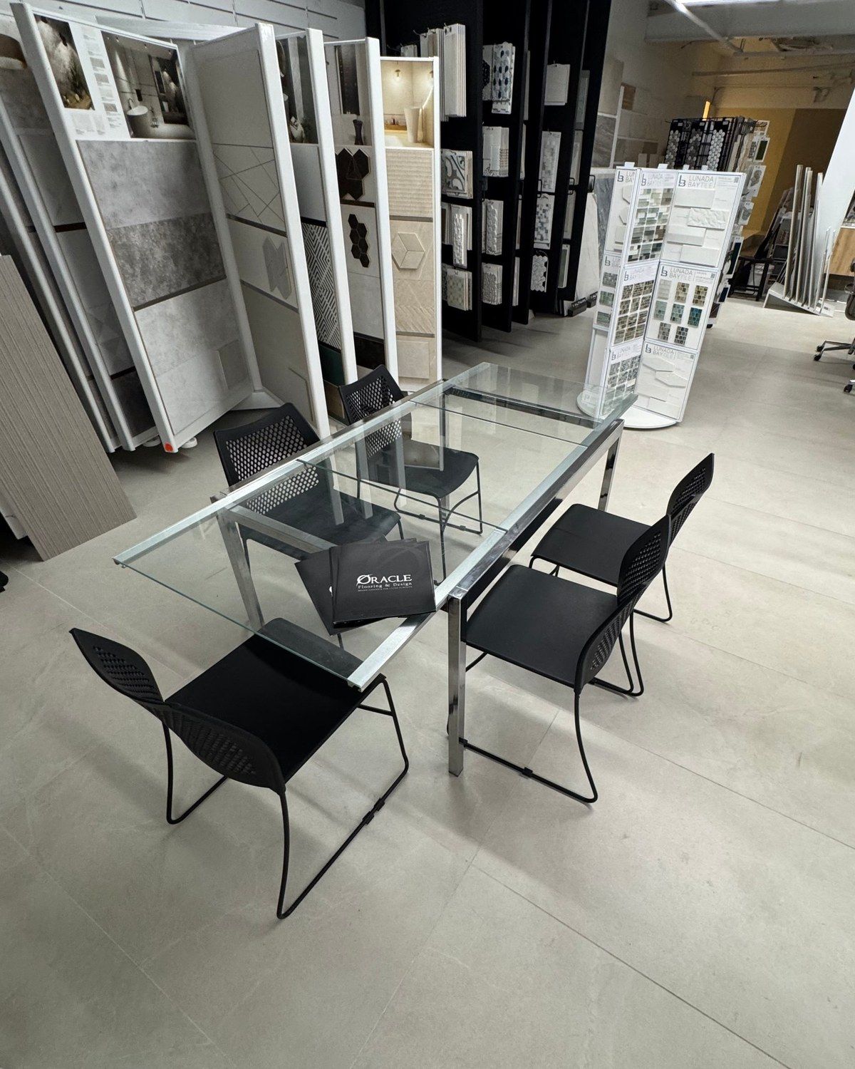 A glass meeting table with Oracle folders in our showroom, beside racks of tile samples